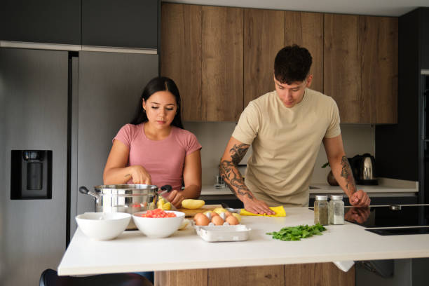 istock Two young latin people peeling potatoes and cleaning kitchen counter at kitchen. 1447347202