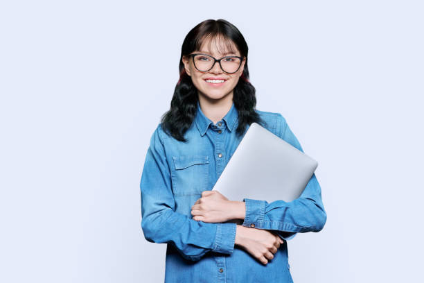 Teenage female student with laptop, looking at camera on light background stock photo