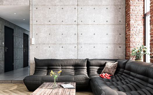 Modern industrial living room with black leather sofa, coffee table, and decoration (vase with flowers, books, remote control, blanket, pillow, potted plant) on the hardwood floor in front of a large concrete and partly ruined brick wall with high windows and copy space. A peek at a hallway with doors leading to other rooms. 3D rendered image.