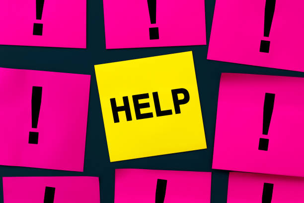 istock Help needed message asking for support, advice, assistance or helping hand to assist in a difficult situation. FAQ concept. Yellow sticker is the center of attention among pink note papers 1447348806