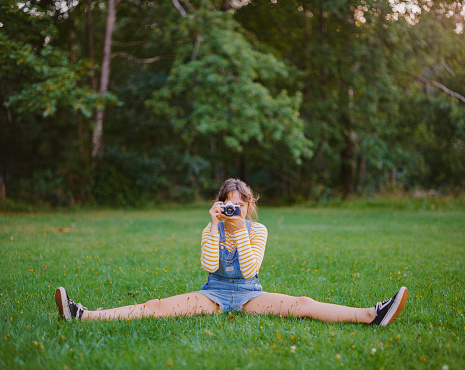 Young Caucasian woman sitting on the lawn and photographing with vintage camera