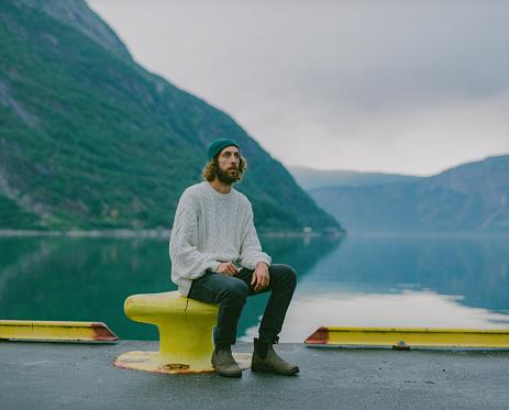 Young Caucasian man sitting on the background of the fjord