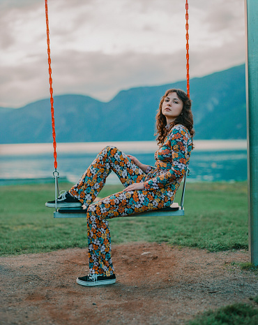 Young Caucasian woman sitting on swing on the background of the fjord