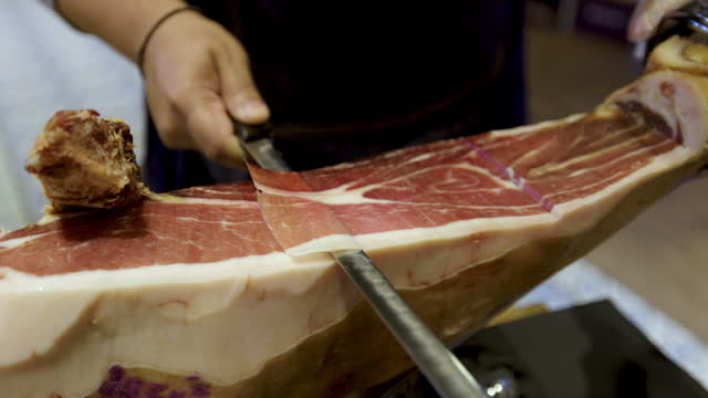 Close up of a man slicing a leg of prosciutto at the delicatessen