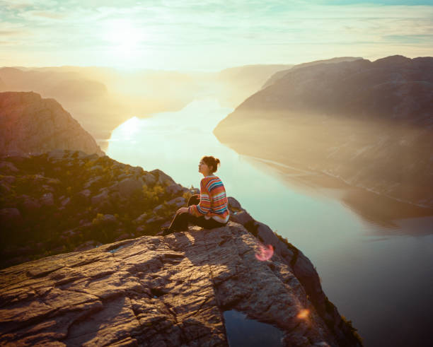 frau sitzt in den bergen vor dem hintergrund des lysefjords - mountain mountain range norway fjord stock-fotos und bilder