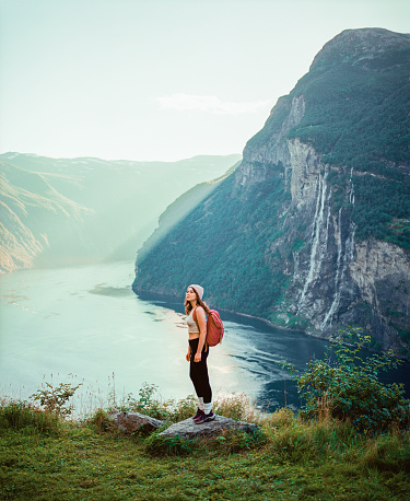 Scenic view of  young Caucasian woman hiking near Seven sisters  waterfall in mountains in Norway