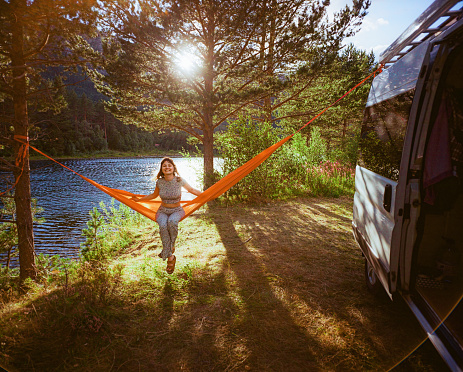 Young Caucasian woman resting in hammock near camper van in forest