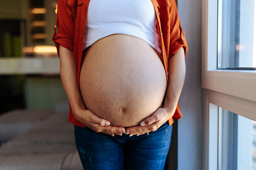 A pregnant Caucasian woman is holding her stomach with her hands.