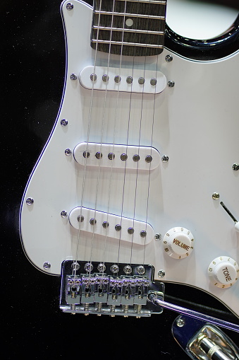 A close up photograph of a sunburst finish solid body electric guitar with three pick ups a whammy bar and volume and tone controllers.