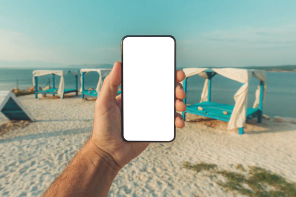 istock Mobile smart phone with blank mockup template screen in male hand, beach pergola in background 1447366524