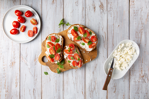 Sandwich with cottage cheese, tomatoes and basil on white wooden background. Traditional Italian bruschetta. Healthy savory feta and tomato toast. Top view.