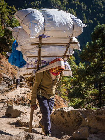Nepalese man carrying heavy load using traditional doku headband up the rocky trail to Everest Base Camp, high in the Himalaya mountains of Nepal.