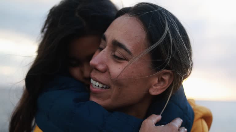 Latin mother having tender moment with her daughter on the beach at sunset during winter time