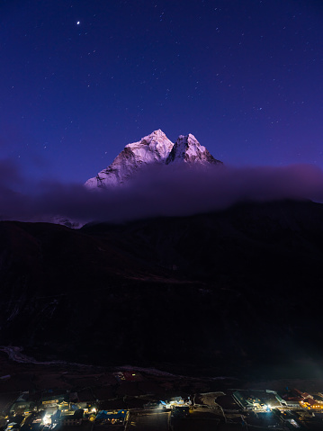 Stars shining above the snow capped peak of Thamserku overlooking the Sherpa teahouses in the Khumbu valley high in the Himalayan mountains of Nepal.