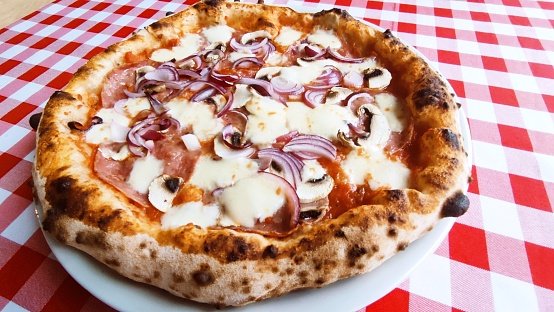 Neapolitan pizza with salami and onions on the Red tablecloth