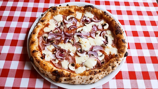 Neapolitan pizza with salami and onions on the red tablecloth