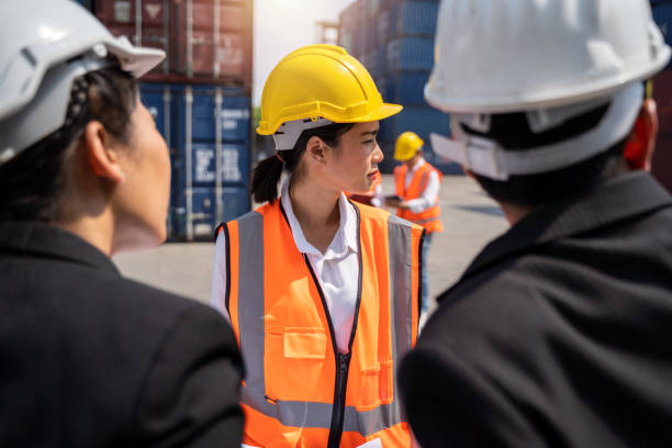 mulher trabalhador trabalhando com foreman, de pé com um capacete amarelo para controlar o carregamento e verificar uma qualidade de contêineres de cargueiro cargo para importação e exportação em estaleiro ou porto - industrial ship dock worker engineer harbor - fotografias e filmes do acervo