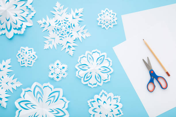 istock Different white snowflake shapes created from paper on light blue table background. Pastel color. Closeup. Top down view. Handmade decoration elements for winter festive. 1447390613