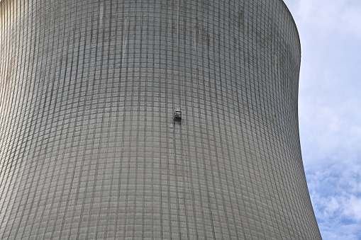 Huge cooling tower of a nuclear power plant with small door in the middle observed from vicinity. Can be used as a background with a lot of copy space.
