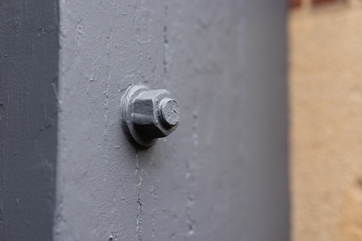 End of a screw with a fastening nut in a gray painted support beam.