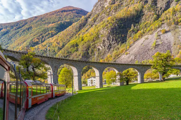 BRUSIO, SWITZERLAND - OCTOBER 28,2022: Bernina Express of Rhaetian Railway Line at the Brusio spiral viaduct on a autumn day in italian Switzerland