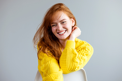 Pleased confident young redhead woman with a beaming smile and folded arms posing on a blue studio background with copy space grinning at the camera. Portrait of positive pretty young woman smiling and looking at camera