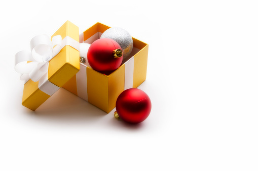 Opened yellow gift box with red, white and silver Christmas decorations. Copy space. White background. No people. Horizontal orientation.