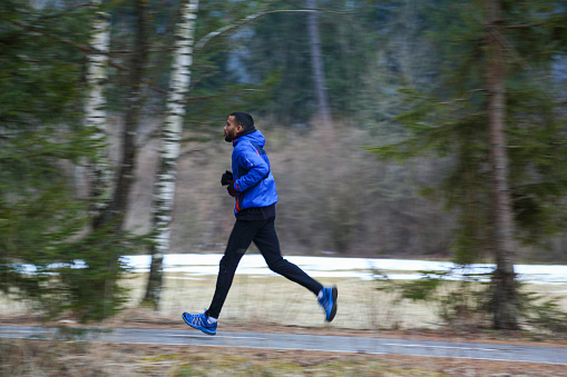 Man in sports clothing running in winter. Snow on road and fog in the park. Motion blur, panning.
