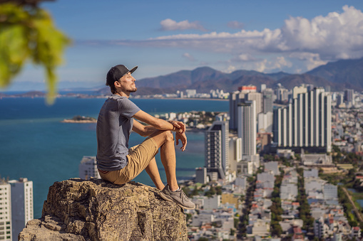 A young man local tourist sits on a rock and enjoys the view of her city. Local tourism concept. Tourism after COVID 19.