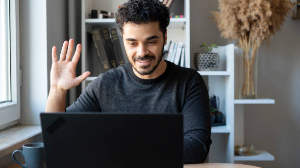 istock Young man video chatting with laptop and greeting 1447398395