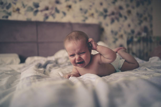 charming baby, 6 months old, crying,on his stomach charming baby, 6 months old, lies crying on his stomach on a bed in a bright, real interior, a childhood end, and teeth are cut, colic of newborns. half dozen babies stock pictures, royalty-free photos & images