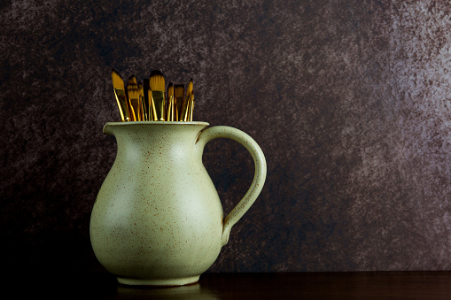 Earthenware jug and artists paint brushes on a polished wooden shelf