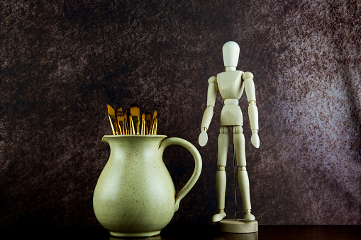 Earthenware wine jug with artists paint brushes and mannequin on a polished wooden shelf