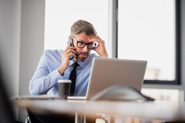 istock Confident businessman making a call while sitting at the office and using laptop 1447399707