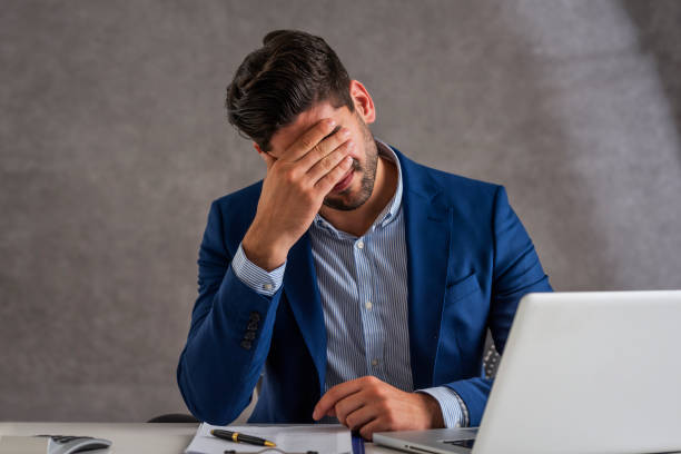 Businessman suffering from strong pain in his head while sitting at office desk Shot of stressed businessman sitting at desk in office with laptop. Professional man suffering from migraine. facepalm stock pictures, royalty-free photos & images