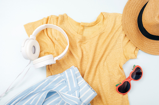 Women's summer clothes, accessories, headphones, straw hat and sunglasses on white background. Beauty, fashion, summer vacation concept. Top view, flat lay.