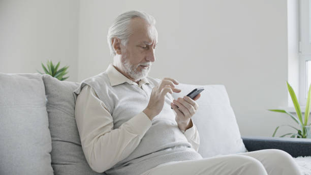 istock Senior man sitting on sofa at home, texting on smartphone, modern technology user 1447405739