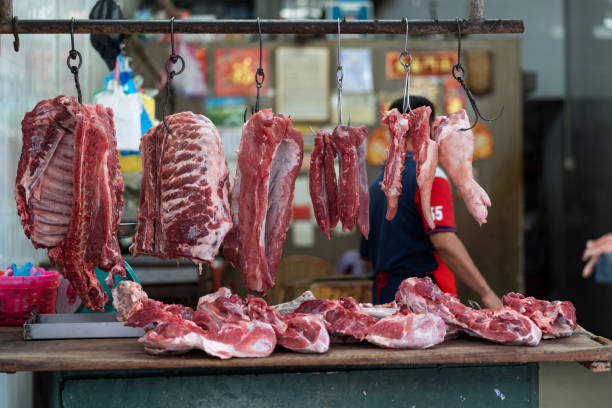 Butcher shop selling pork meat in Penang wet market, with cuts of pork hanging up.