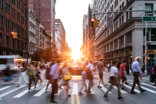 Diverse crowds of people walking through a busy intersection on 5th Avenue and 23rd Street in New York City with sunset background stock photo