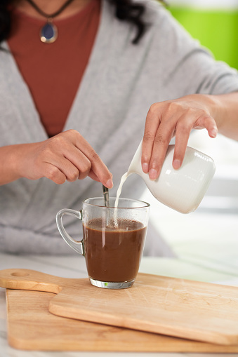 Closeup image of woman adding milk in morning coffee and mixing with spoon