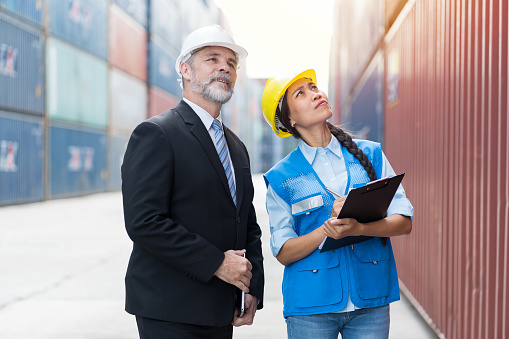 Male and female container yard workers discuss of container boxes from cargo freight ship at commercial dock site. Container boxes transportation or delivery goods concept