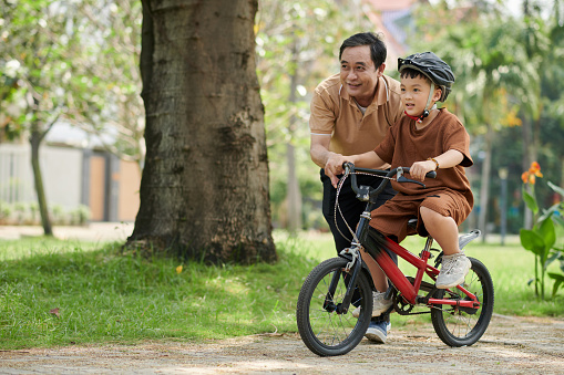 Grandfather teaching little grandson riding bicycle in city park