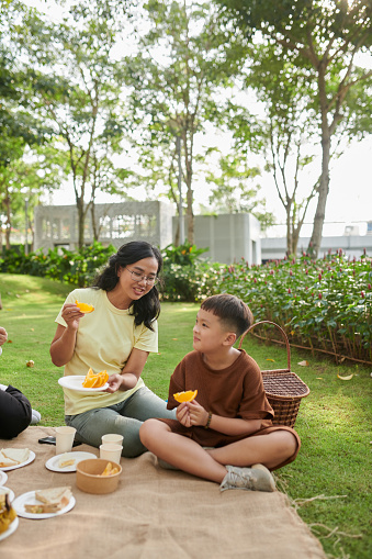 Mother and son eating fresh ripe oranges when enjoying family picnic