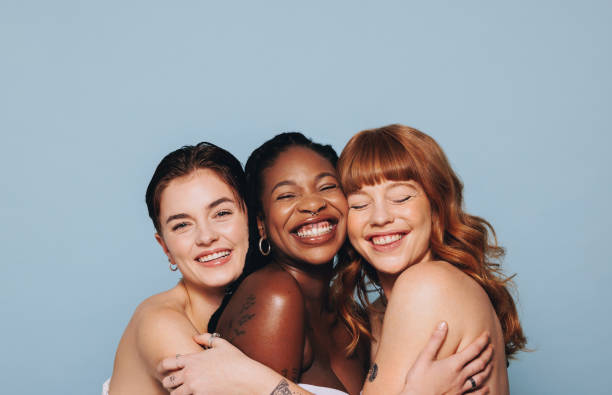 sekelompok wanita bahagia dengan warna kulit berbeda tersenyum dan saling berpelukan di studio - woman skincare potret stok, foto, & gambar bebas royalti