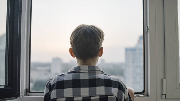 Back view of teen boy looking through window, sad orphan kid waiting on adoption Back view of teen boy looking through window, sad orphan kid waiting on adoption orphan stock pictures, royalty-free photos & images