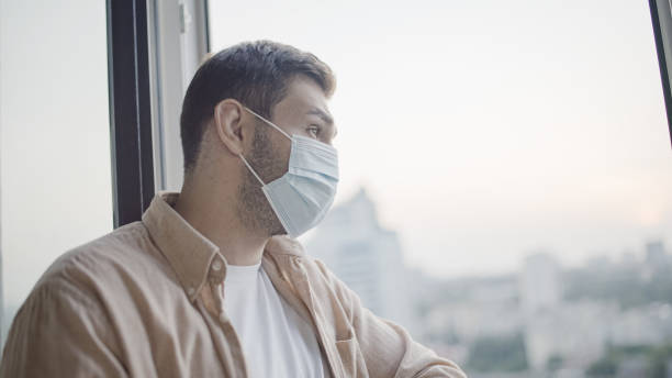 istock Middle-aged man in protective face mask looking out window, pandemic safety 1447417244