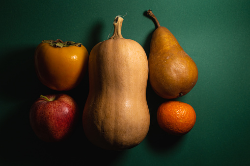 Pumpkin, apple, pear, tangerine and persimmon on a green background