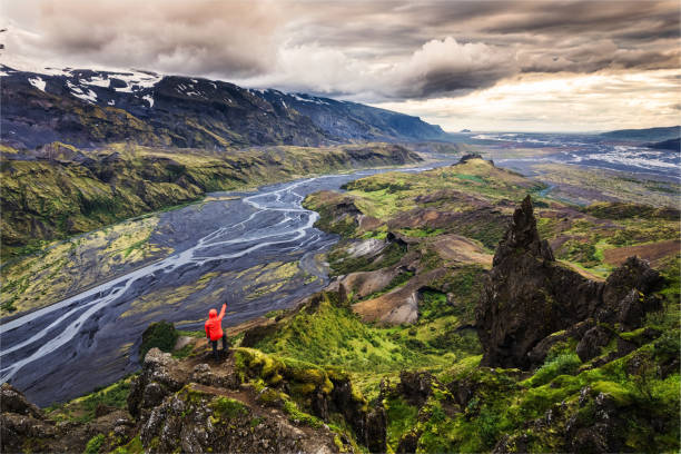 Hiker man in red jacket standing on peak of Valahnukur viewpoint with mountain valley and krossa river in icelandic highlands at Thorsmork, Iceland stock photo