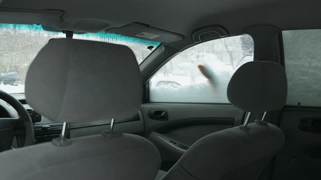 The owner of the car cleans the window of the front door of the car from snow.