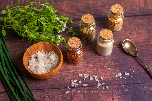 Spices in small bottles, salt, basil and chives on a wooden table